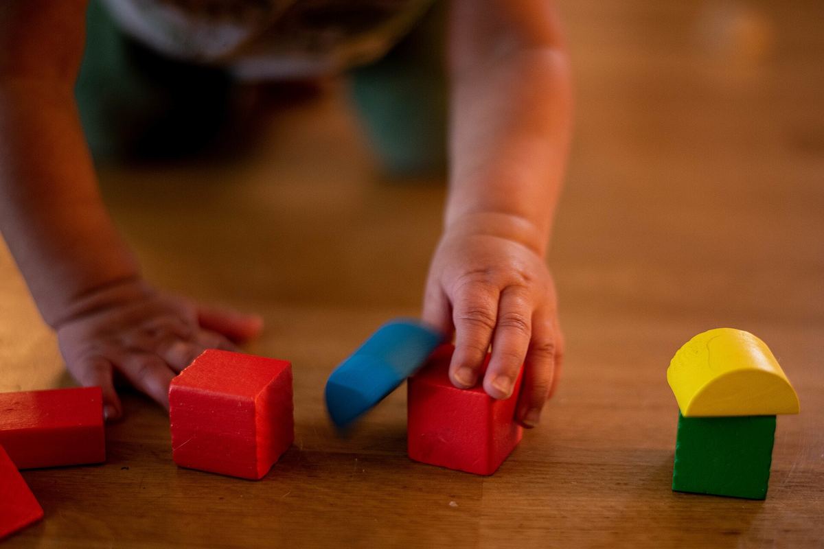 A toddler's hands arranging wooden blocks on a floor